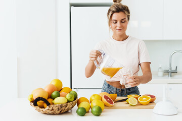 Wall Mural - Woman pouring freshly squeezed homemade orange juice into the glass in modern white kitchen