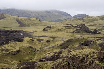 Sticker - Moss landscape mountains against the foggy sky and a car below in Iceland