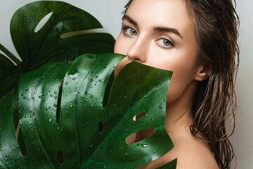 Wall Mural - young woman with a smooth skin holding monstera deliciosa plant leaf
