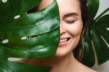 Wall Mural - young woman with a smooth skin holding monstera deliciosa plant leaf