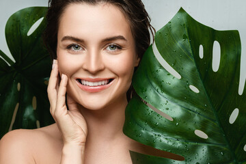 Wall Mural - young woman with a smooth skin holding monstera deliciosa plant leaf