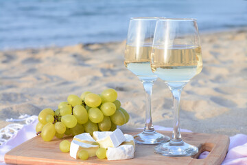 Wall Mural - Glasses with white wine and snacks for beach picnic on sandy seashore