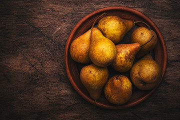 Wall Mural - Autumn harvest of yellow pears on clay plate on old rustic wood kitchen table background, top view