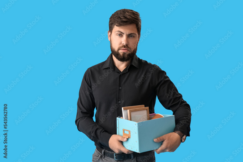 Fired young man holding box with his office stuff on blue background