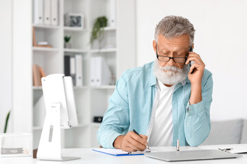 Sticker - Senior man talking by mobile phone and writing at table in office