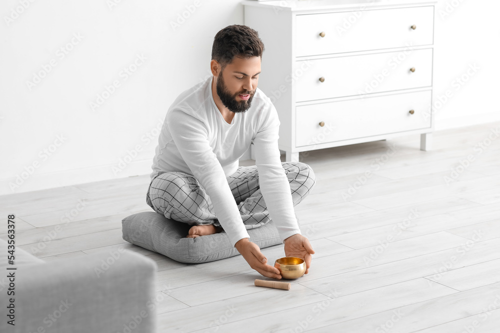 Young man with Tibetan singing bowl sitting at home