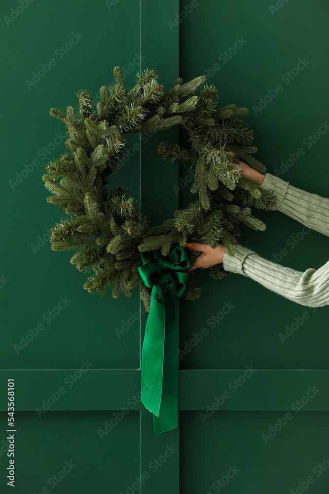 Female hands with beautiful Christmas wreath on color wall