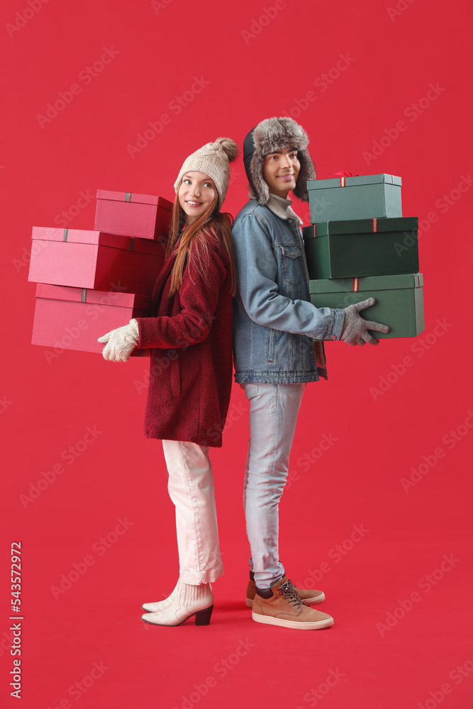 Happy young couple with Christmas presents on red background