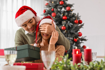 Canvas Print - Young man surprising his beloved wife with gift in kitchen on Christmas eve