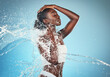 Beauty, skincare and splash with water and black woman shower, hydration and moisture body care. Spa, wellness and health with girl model for luxury, natural and cosmetics in blue background studio