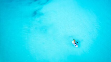 Wall Mural - aerial top down view of a woman on a stand up paddle (sup) board over the turquoise caribbean ocean 
