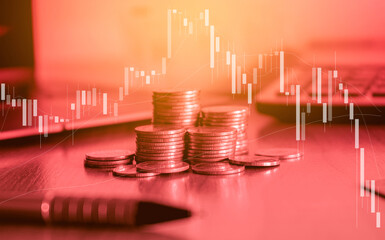 Stack of money coin on office desk with trading graph. Business and financial concept with red filter.