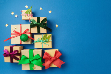 Wall Mural - Christmas gift boxes with colorful ribbons on blue background in shape of Christmas tree. Holiday wrapping and packaging concept. Top above. Flat lay