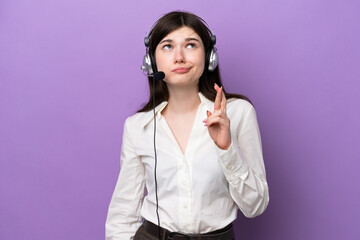 Wall Mural - Telemarketer Russian woman working with a headset isolated on purple background with fingers crossing and wishing the best