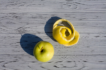 Ripe green whole apple and trimmings after peeling the apple lie on a light textured wooden table in the kitchen.