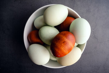 Wall Mural - Blue, Green, and Brown Heritage Eggs In a Bowl On a Rustic Background: Overhead view of a group of multicolored eggs on in a small bowl