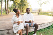 © BullRun - Cheerful black couple having conversation while sitting on wooden walkway