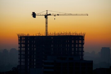 Canvas Print - Sunrise behind the silhouette of a construction site with a crane