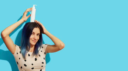 Wall Mural - Young beautiful woman with blue hair holding white cosmetic bottle on bright background