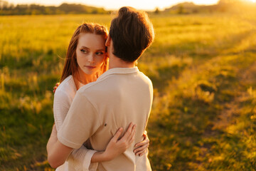 Wall Mural - elegant ginger young woman and unrecognizable man in love embracing, bonding, stroking standing toge