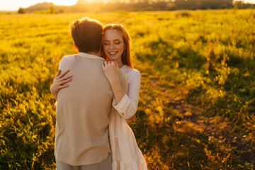 Wall Mural - smiling red-haired young woman with closed eyes in dress and man in love embracing, bonding, strokin