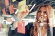 © Kostiantyn - Businesswoman writing on sticky notes on glass wall while working in office
