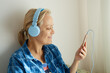 © evafesenuk - Close-up joyful mature woman in blue headphones uses smartphone