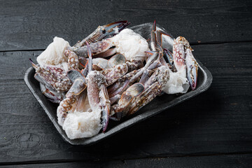 Wall Mural - Frozen raw  blue swimming crab parts, in plastic tray, on black wooden table background