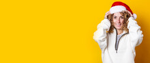 Cheerful Curly Young Woman Wearing Santa Claus Hat On A Yellow Background. Banner.