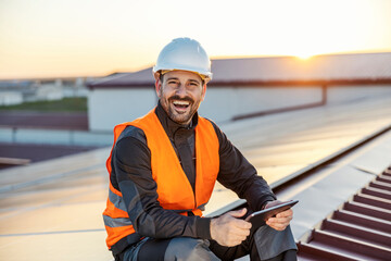 Wall Mural - Portrait of happy worker with tablet checking on solar panels on the roof.