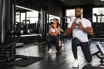 Wall Mural - Fitness couple, african man and caucasian woman, in sportswear doing squat exercises at gym.