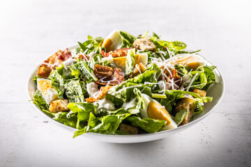 Wall Mural - Caesar salad prepared from romaine lettuce, baked bacon, egg, bread croutons, garlic dressing and grated Parmesan cheese on white table.