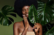 © Beauty Agent Studio - Organic cosmetic concept. Green beauty portrait. Young African American woman smiling and holding banana leaf against tropical green leaf. Natural cosmetics concept.