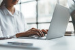 © amnaj - Close-up of the hands of a business woman attentively typing on a laptop computer and having a document on the desk in the office.