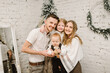 © Serhii - Father, mother hugs son and daughter stand near Christmas tree at home. Mom, dad with kids. Happy New Year and Merry Christmas. Christmas decorated interior. The concept of family holiday. Closeup.