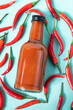 Hot chili sauce in a bottle on a bright blue background with fresh red pepper. The concept of vegetarian delicious food.