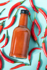 Wall Mural - Hot chili sauce in a bottle on a bright blue background with fresh red pepper. The concept of vegetarian delicious food.