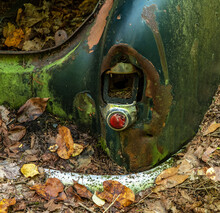 Broken Rear Light Of Abandoned Vintage Car With Leaves All Around
