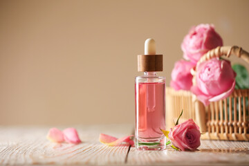 Bottle of essential rose oil and flowers on white wooden table against beige background, space for text