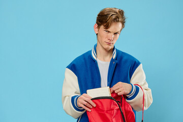 Wall Mural - a young student in a bomber jacket takes out a notebook from his backpack looking at the camera