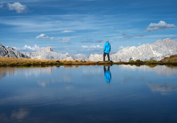 Wall Mural - man and mountains reflected in lake at sunset in autumn in dolomites, italy. standing guy on the sho