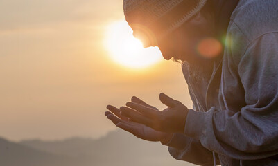 Wall Mural - Human with hands open palm up praying to God on the mountain sunset background.