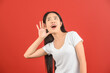 © Johnstocker - Portrait of Young asian woman in white t-shirt puts a hand to the ear to hear better isolated on red background
