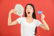 © Johnstocker - Portrait of a cheerful young woman holding money banknotes and credit card isolated over red background