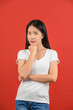 © Johnstocker - Portrait of distrustful young asian woman in white t-shirt hand chin isolated on red background