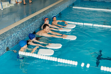 Wall Mural - A group of boys and girls train and learn to swim in a modern swimming pool with an instructor. Development of children's sports. Healthy parenting and promotion of children's sports.