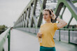 Young woman drinking water and listening music trough headphones, during jogging in city, healthy lifestyle and sport concept.