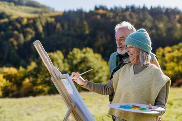 Wall Mural - Senior couple painting together in nature, during autumn day.