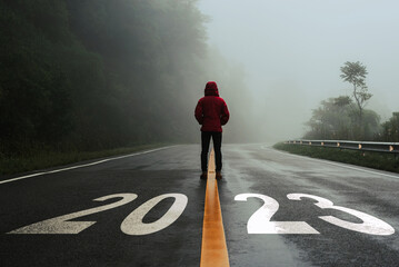 Man standing alone on the road and looking at target with text 2023 written on the road in the middle of asphalt road with at sunset. Concept of planning, goal, challenge, new year resolution..