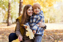 Cute Boy With Mother Holding Yellow Leaves In Park